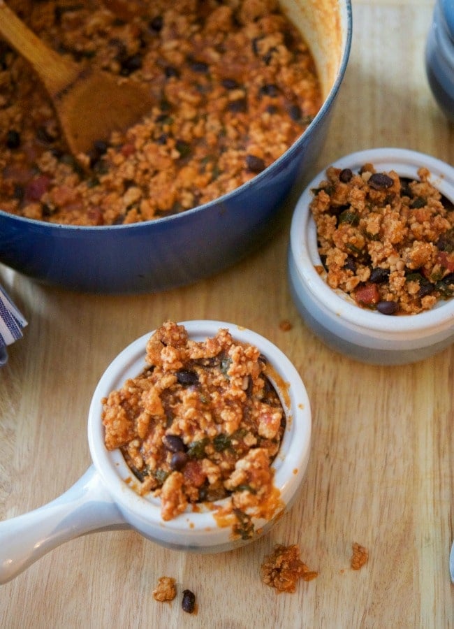 A bowl of food sitting on top of a wooden table, with Bean and Chicken