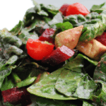 A close up of spinach salad on a white plate with description.