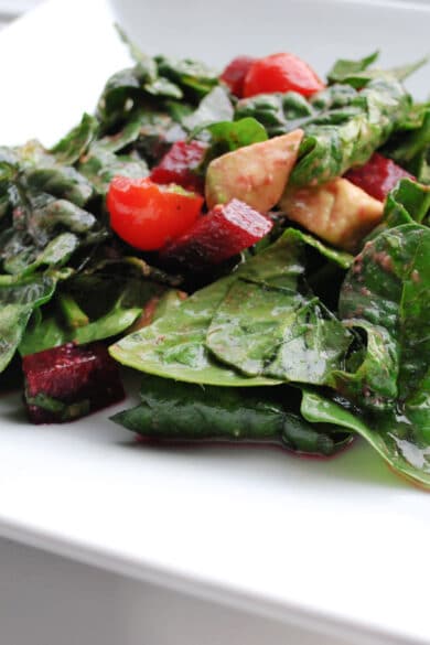 A close up of spinach salad with beets and avocado on a white plate.