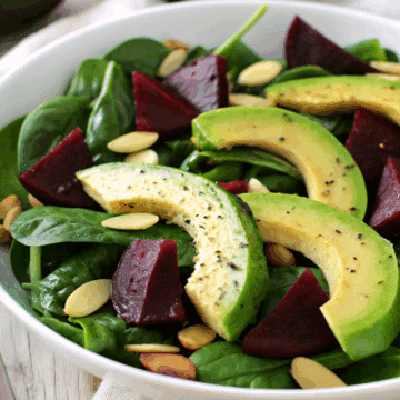 a close up of a bowl of spinach salad with avocado and beets