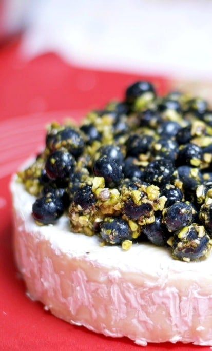 A close up of blueberries and pistachios on top of Brie cheese. 