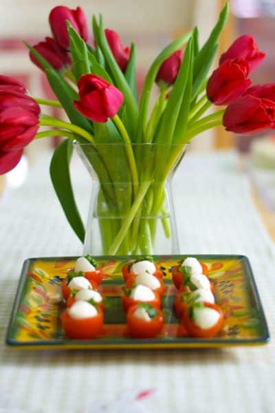A vase of flowers on a table with Cherry Tomato Bites on a plate