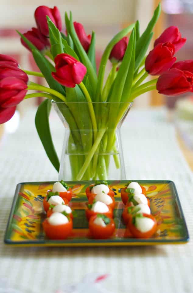 A vase of flowers on a table with Cherry Tomato Bites on a plate