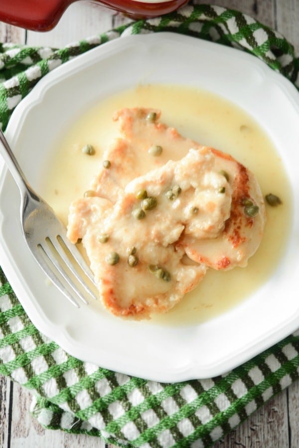 Boneless chicken topped with a piccata caper sauce on a white plate. 