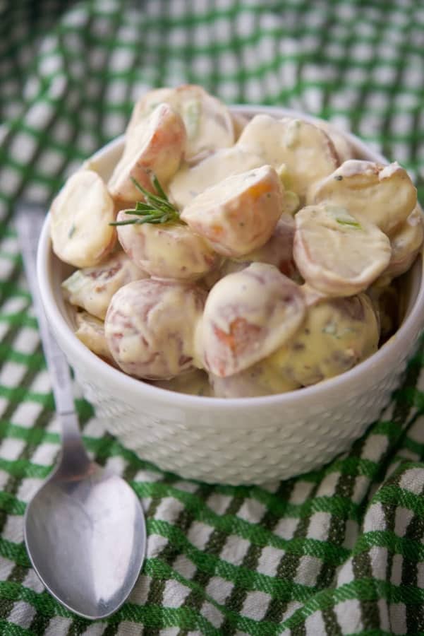 Baby red bliss potatoes tossed with Dijon mustard, mayonnaise and fresh rosemary in a bowl. 