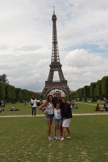 A group of people standing on top of a grass covered field with Eiffel Tower in the background