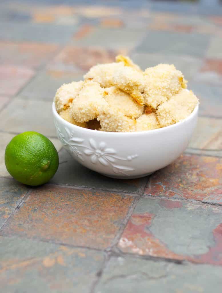 Lime chicken nuggets in a white bowl on top of a table with a lime. 