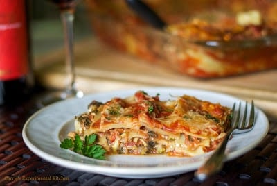 A plate of food and a glass of wine, with Cheese and Vegetable lasagna