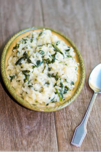 A close up of spinach risotto in a dish with a spoon.