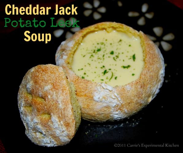 Close up of Cheddar Jack Potato Leek Soup in a soup crock on a wooden table. 