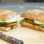A cut in half sandwich sitting on top of a wooden cutting board, with Chicken and Cheese