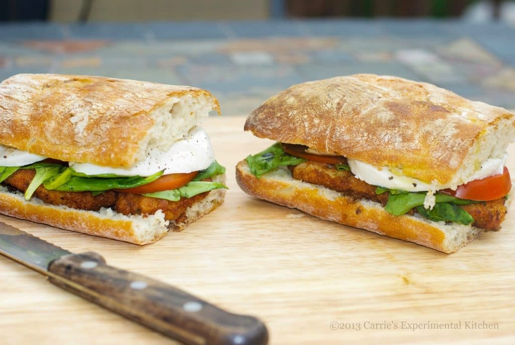 A cut in half sandwich sitting on top of a wooden cutting board, with Chicken and Cheese