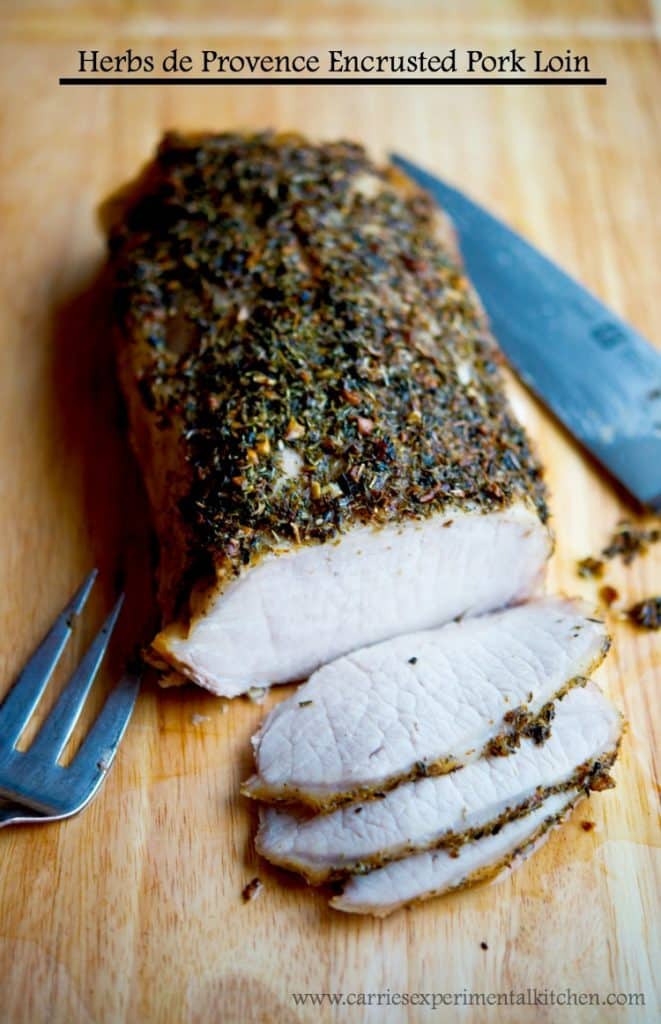 A close up of sliced Herbs de Provence Encrusted Pork Loin on a wooden cutting board.