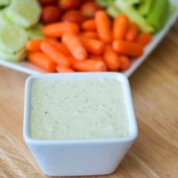 A bowl of food sitting on top of a wooden cutting board, with Crudite dip and Dipping sauce