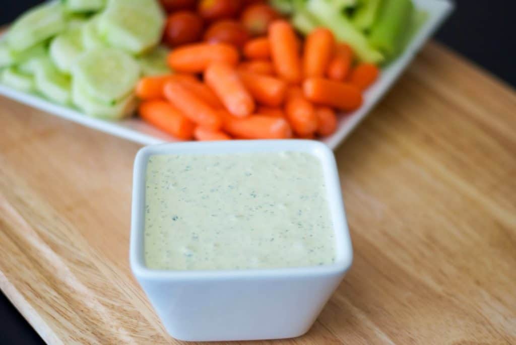 A bowl of food sitting on top of a wooden cutting board, with Crudite dip and Dipping sauce