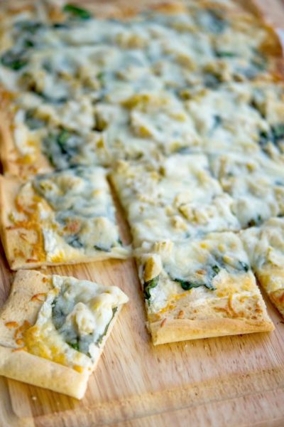 A slice of pizza sitting on top of a wooden cutting board, Spinach & Artichoke Flatbread