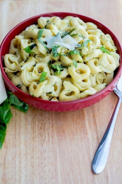 A bowl of food on a wooden table, with tortellini pasta