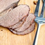 Beef brisket sliced on a cutting board with a fork