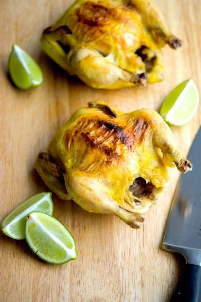 Tarragon Lime Cornish Hens sitting on a wooden cutting board with limes and a knife.