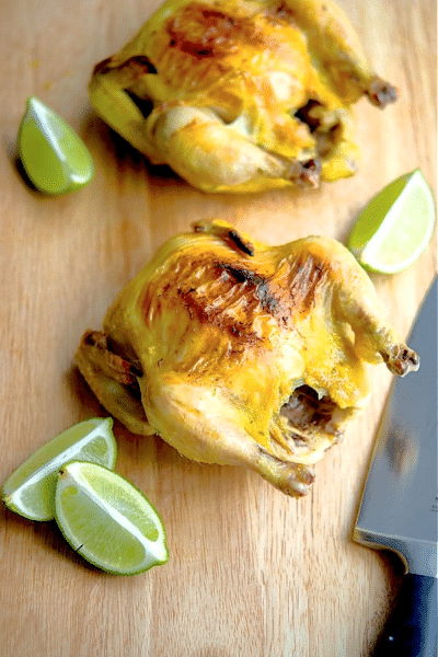 two cornish hens on a cutting board with limes