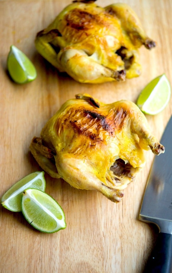 Tarragon Lime Cornish Hens sitting on a wooden cutting board with limes and a knife. 
