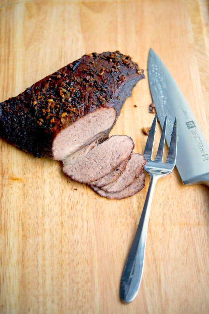 A knife sitting on top of a wooden cutting board, with beef brisket