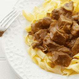 Madeira Beef Stew over egg noodles on a white plate with a fork.