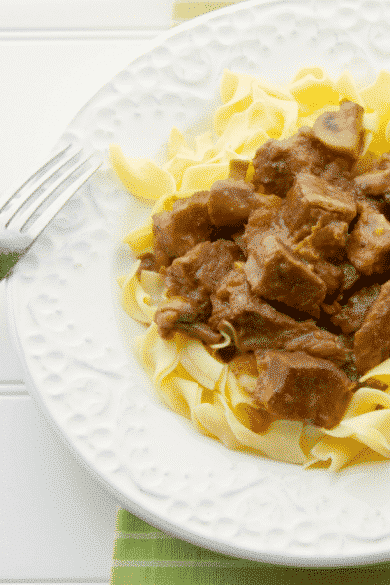 Madeira Beef Stew over egg noodles on a white plate with a fork.