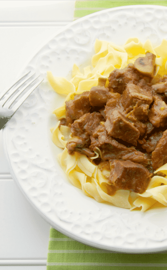 Madeira Beef Stew over egg noodles on a white plate with a fork. 