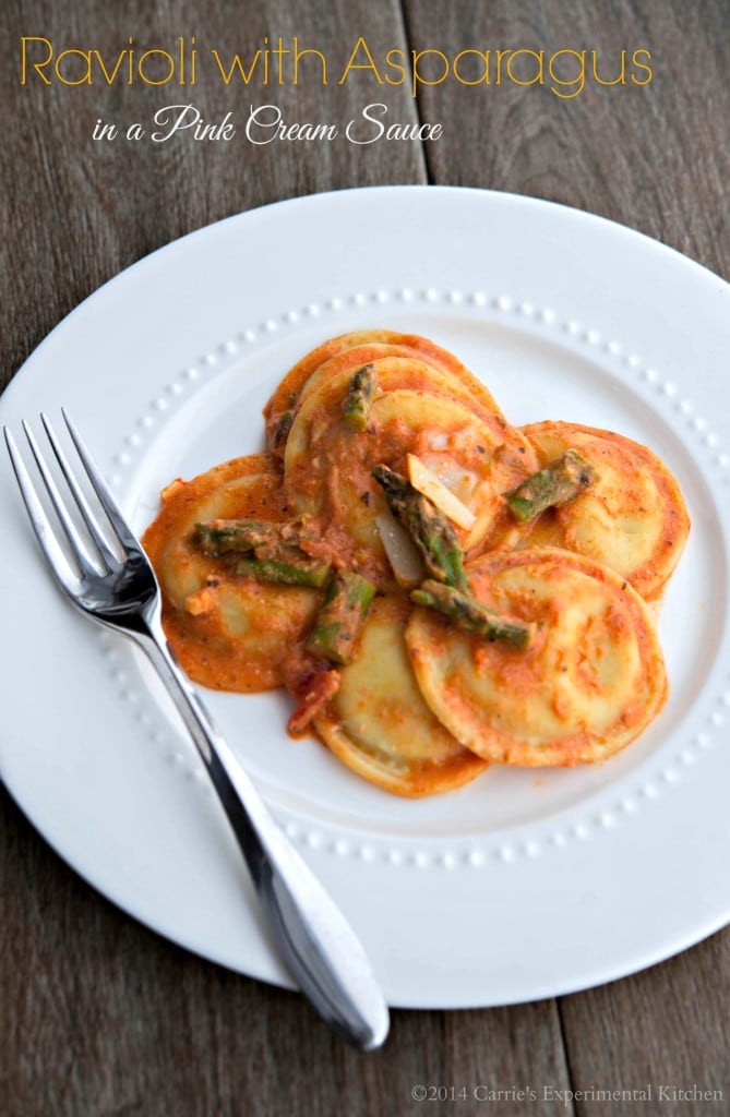 A plate of ravioli with asparagus in a pink cream sauce. 