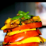 sliced tomatoes and mangoes stacked on a plate