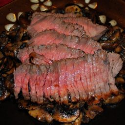 A close up London broil on a plate with mushrooms.