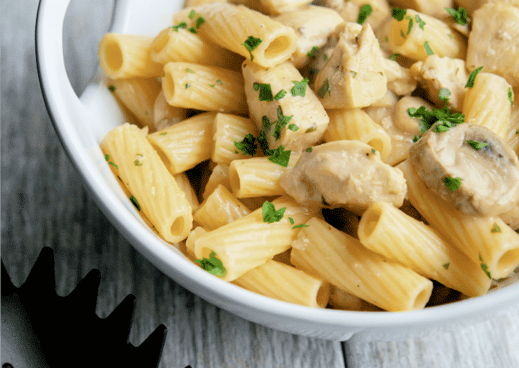 A close up of pasta and chicken in a white bowl