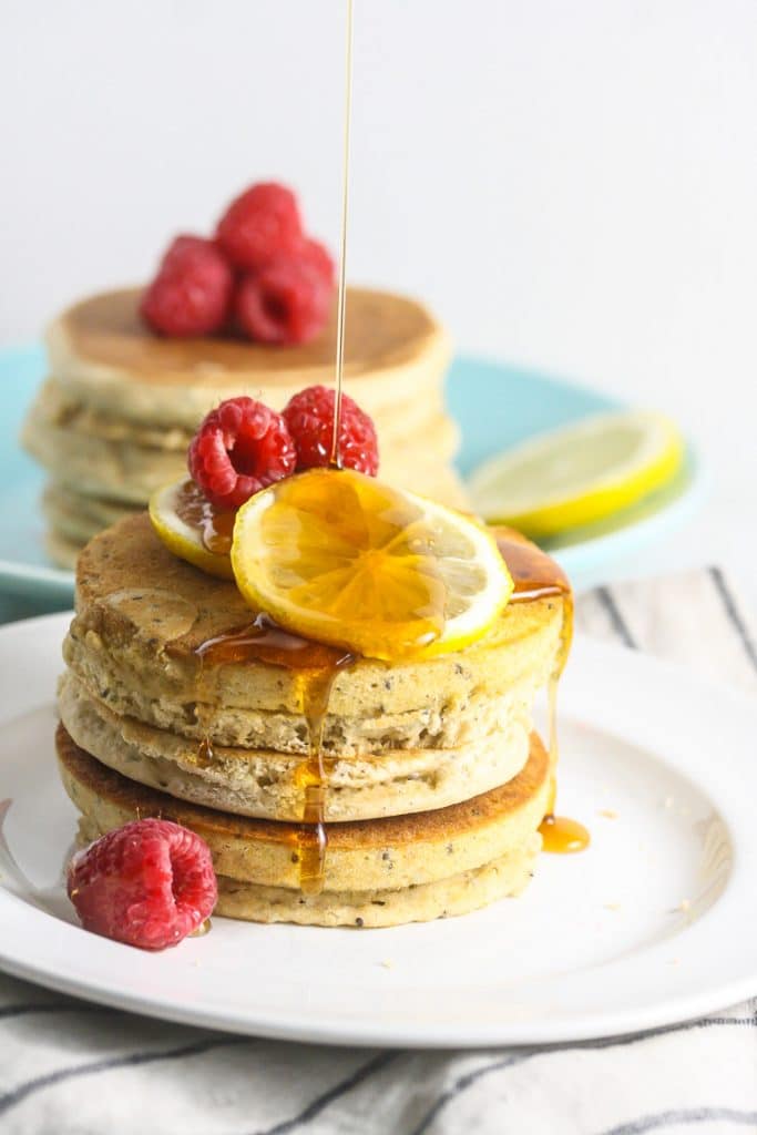 Chia seed pancakes on a plate topped with lemon and raspberries.