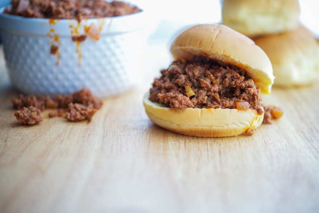 A sandwich on a hamburger bun on a wooden cutting board. 