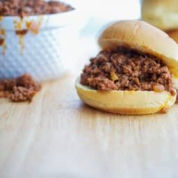 A sandwich on a hamburger bun on a wooden cutting board.