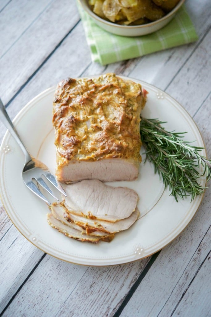 Dijon Rosemary Encrusted Pork Loin sliced on a plate with fresh rosemary.