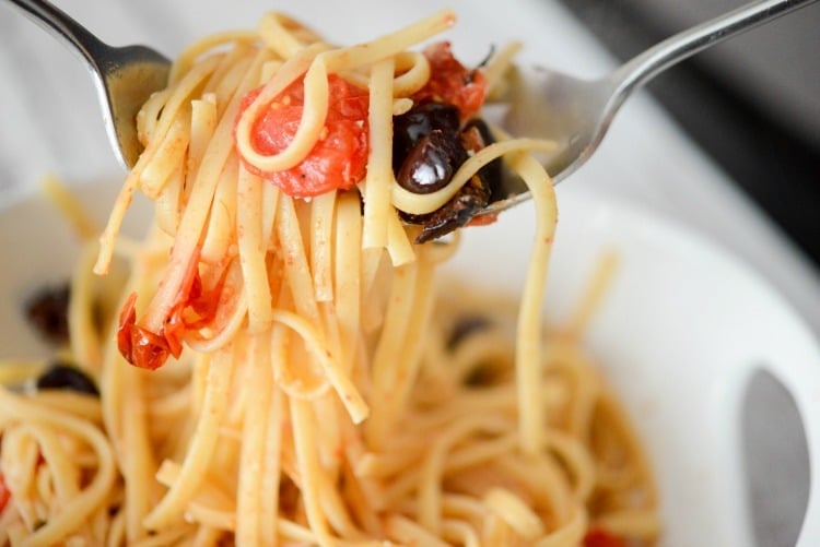 A bowl of spaghetti on a fork with tomatoes and olives. 