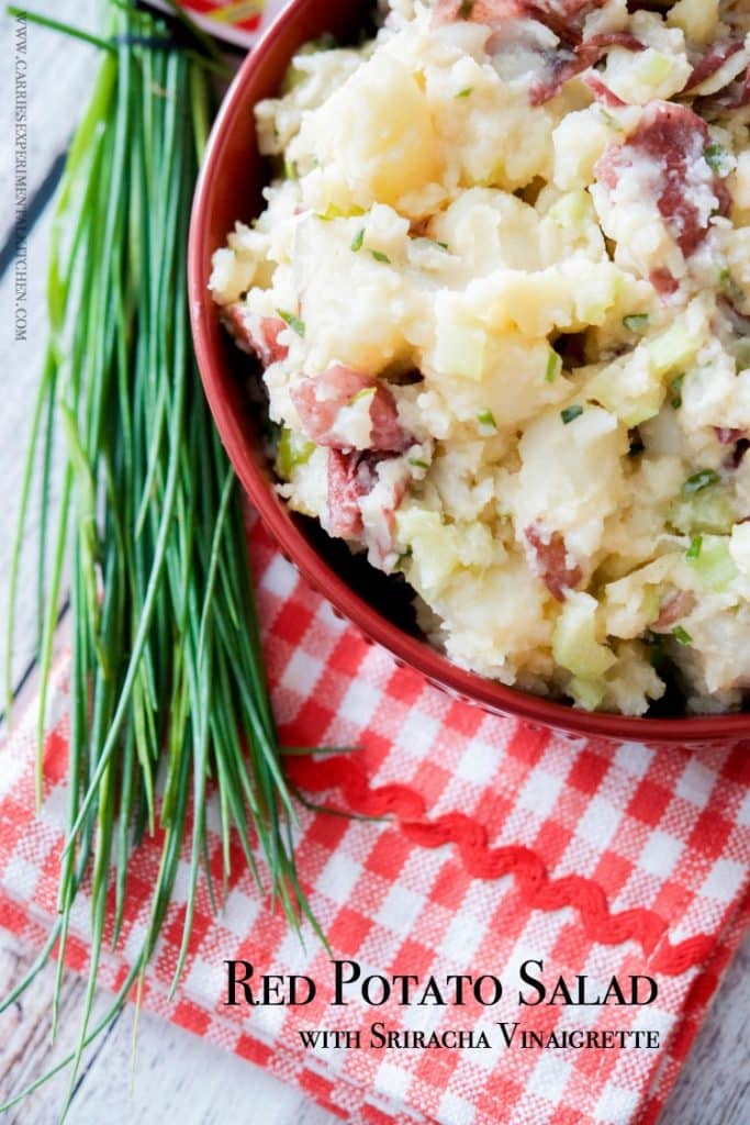Sriracha potato salad in a red bowl with a bunch of chives. 