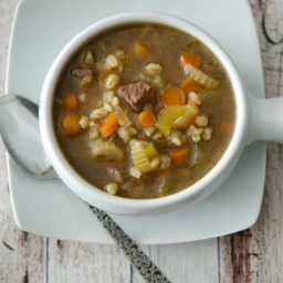 A bowl of soup and a spoon on a table, with Beef barley soup