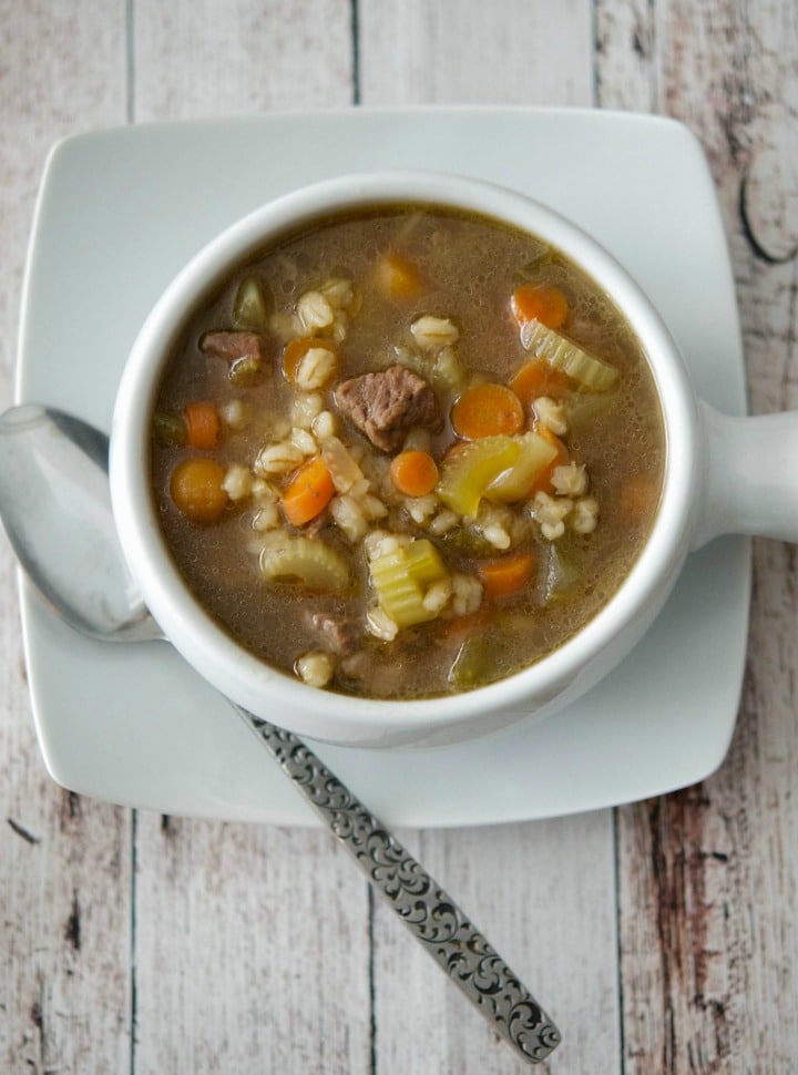 A bowl of soup and a spoon on a table, with Beef barley soup