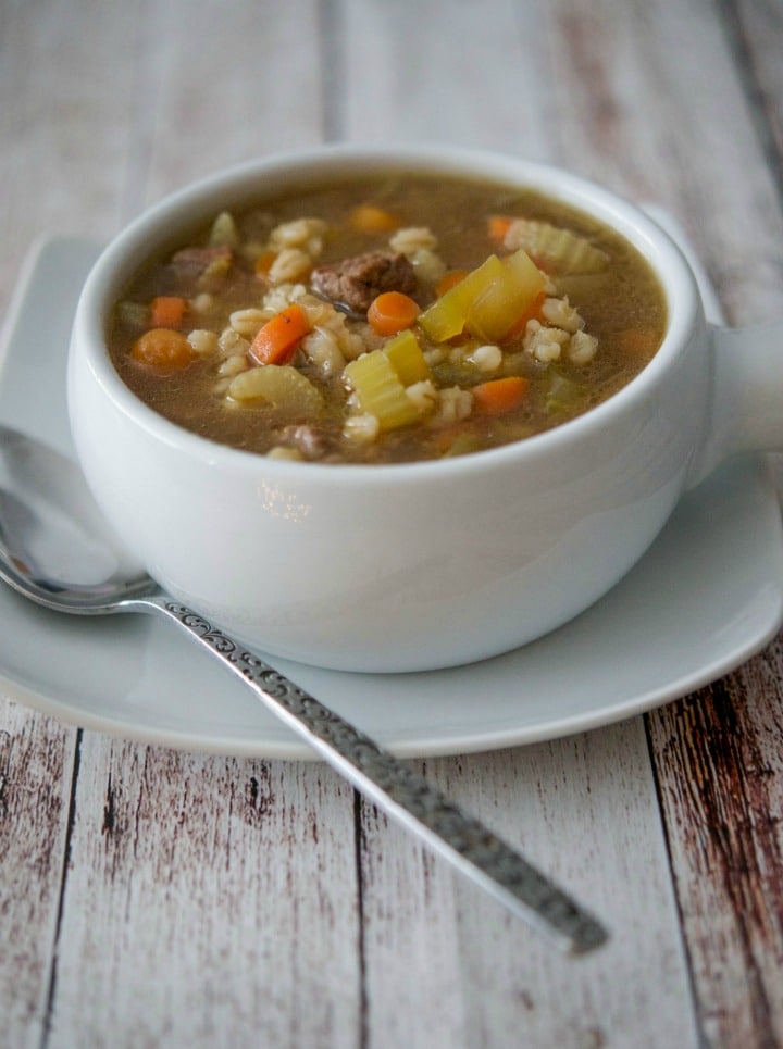 A bowl of soup sitting on top of a wooden table, with Barley and Beef