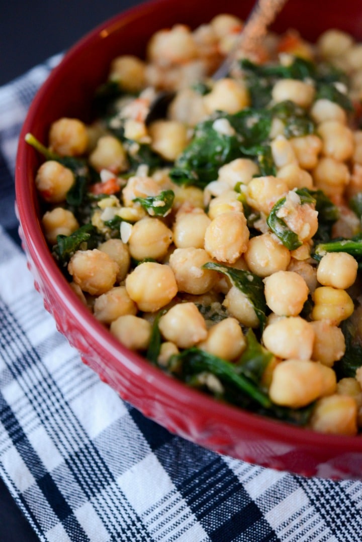 Sautéed chick peas tossed with garlic, diced tomatoes, organic spinach, lemon and vegetable broth in a bowl.