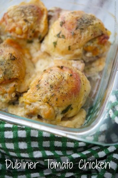 A close up of chicken thighs with tomatoes and Dubliner cheese in a glass baking dish.