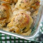 A close up of chicken thighs with tomatoes and Dubliner cheese in a glass baking dish.