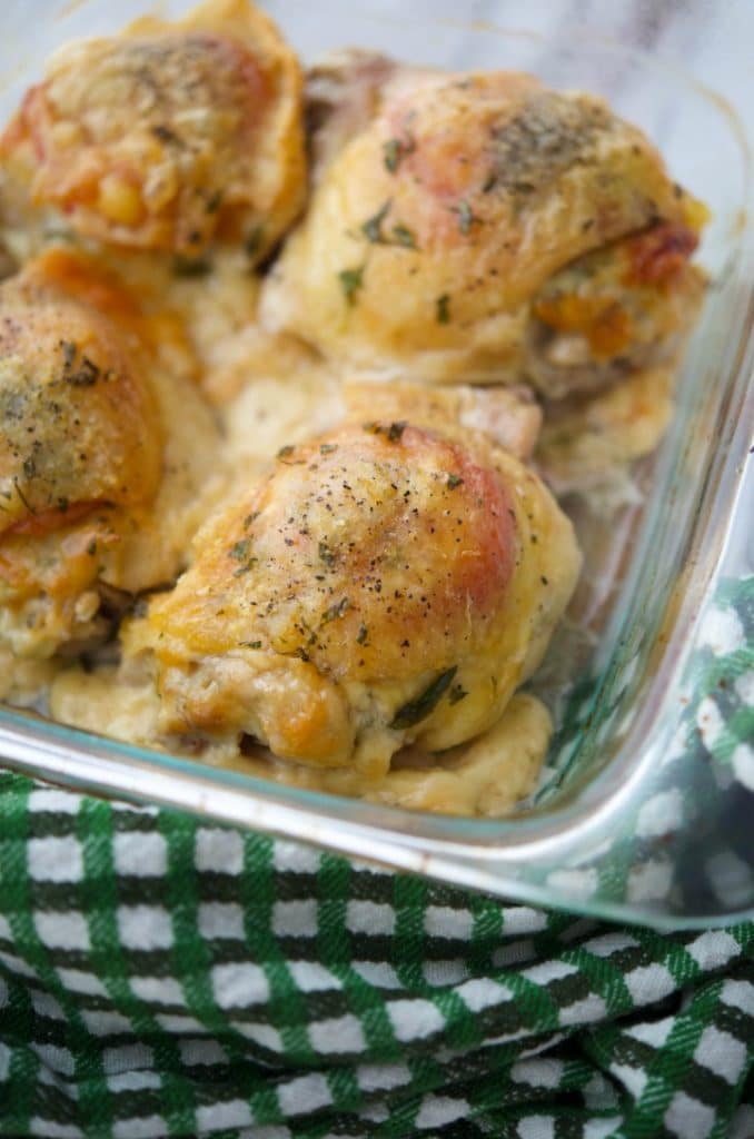 A close up of chicken thighs with tomatoes and Dubliner cheese in a glass baking dish. 
