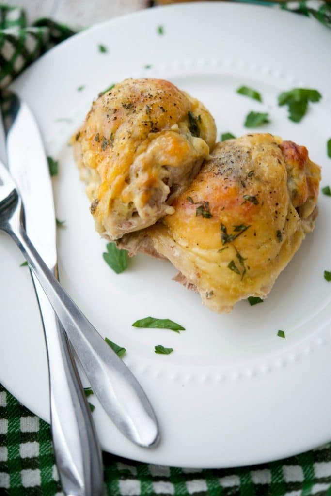 A close up of chicken thighs with tomatoes and Dubliner cheese on a white plate. 