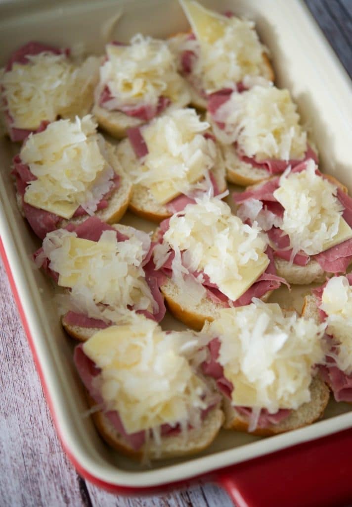 A close up of a pan with corned beef and sauerkraut on the bottom part of a slider roll. 