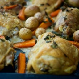 A close up of chicken thighs with potatoes and carrots.