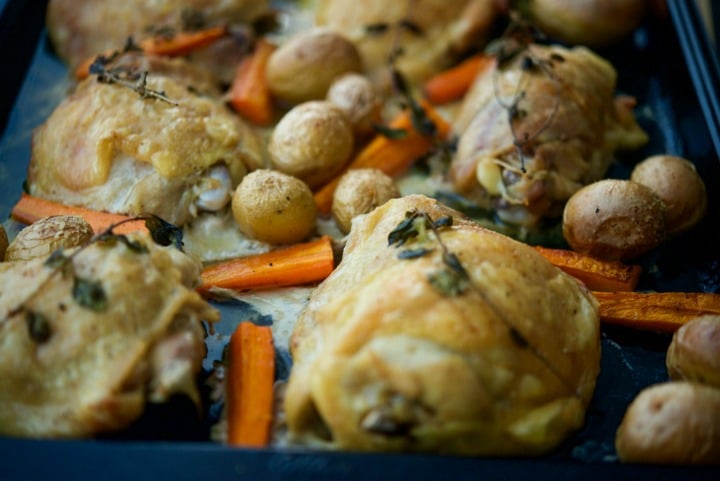 A close up of chicken thighs with potatoes and carrots.